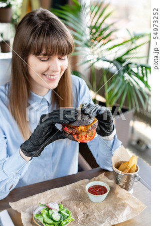 Young woman in blue shirt and black gloves eating delicious juicy hamburger with beef chop. Burgers 54973252