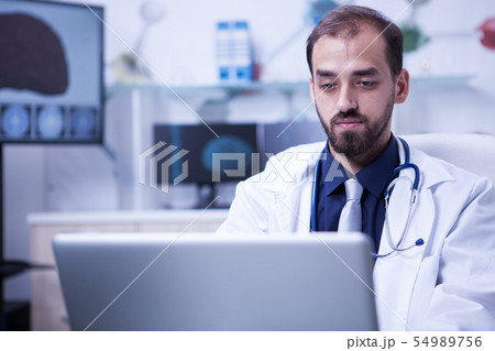 Close up portrait of handsome doctor sitting at his desk and working on computer Close up portrait of handsome doctor sitting at his desk and working on computer 54989756