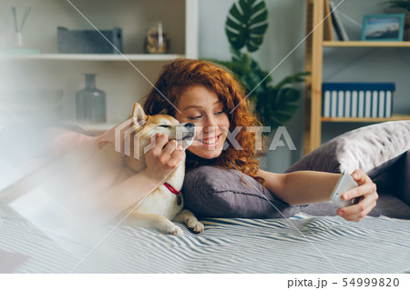 Teenage girl taking selfie with cute puppy using smartphone at home Teenage girl taking selfie with cute puppy using smartphone at home 54999820