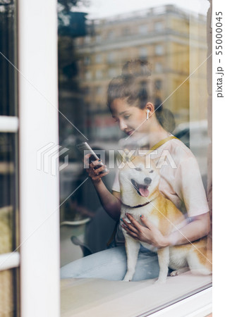 Pretty woman in earphones using smartphone hugging dog in cafe 55000045