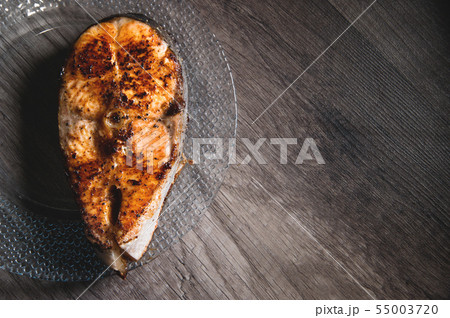 Close-up one grilled cum salmon keta fish steak on a glass transparent plate on a dark wood table 55003720