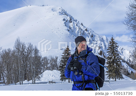 Senior man holding binoculars by snow covered mountain in Sun Valley, Idaho, USA 55013730