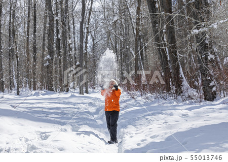 Mature woman wearing orange coat throwing snow by bare trees 55013746