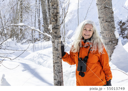 Mature woman wearing orange coat by bare trees in snow 55013749