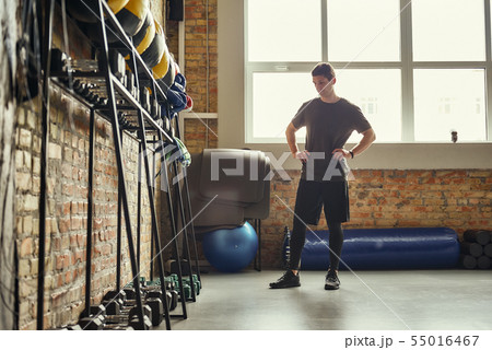 Ready for workout. Confident young man is looking at sport equipment while exercising at gym. 55016467