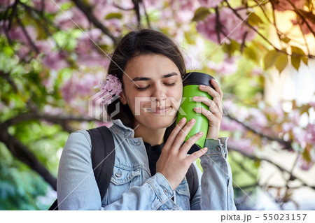 Young smiling woman hold green bottle on the background of blooming sakura 55023157