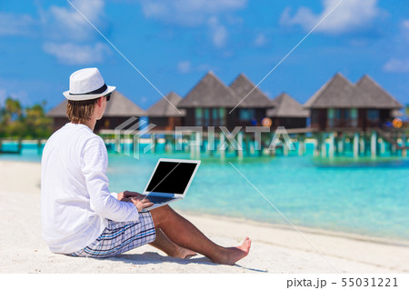 Young man with laptop at tropical beach near water villa 55031221