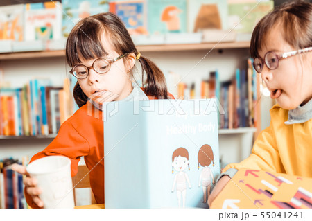 Unusual young girls sitting together and observing informative book Unusual young girls sitting together and observing informative book 55041241