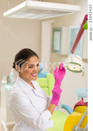 Beautiful smiling dark-haired doctor putting on aseptic gloves Beautiful smiling dark-haired doctor putting on aseptic gloves 55043435