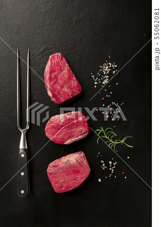 Raw fillet beef steaks with salt, pepper, rosemary, and a carving fork on a black background with 55062081