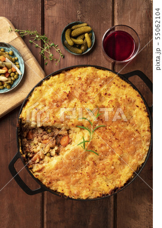 Cottage pie with pickles and red wine, overhead shot on a dark rustic wooden background Cottage pie with pickles and red wine, overhead shot on a dark rustic wooden background 55062104