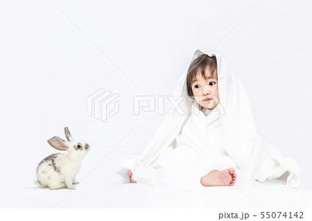 白背景で白いバスタオルを被りウサギの子と遊ぶ女の子の赤ちゃん。幸せ,愛情,赤ちゃん,育児イメージ 55074142