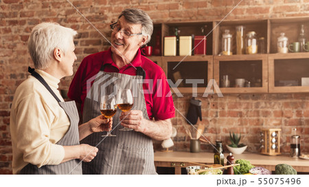Happy married seniors enjoying evening glass of wine at kitchen 55075496
