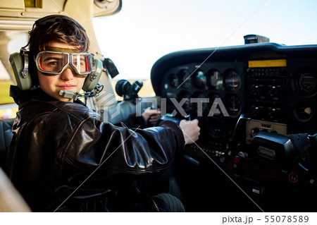 boy dressed in large pilot jacket, headset and aviator glasses, sitting in cockpit boy dressed in large pilot jacket, headset and aviator glasses, sitting in cockpit 55078589
