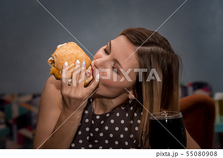 Young woman eating hamburger in restaurant. Close up face with closed eyes Young woman eating hamburger in restaurant. Close up face with closed eyes 55080908