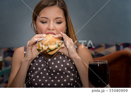 Young woman eating hamburger in restaurant. Close up face with closed eyes Young woman eating hamburger in restaurant. Close up face with closed eyes 55080909