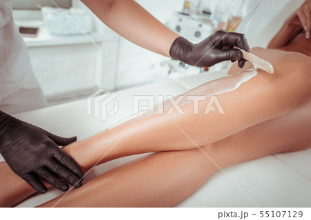 Attentive experienced cosmetologist working with wooden spatula Attentive experienced cosmetologist working with wooden spatula 55107129