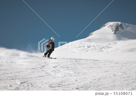 A bearded mature aged male skier in a black ski suit descends along the snowy slope of a ski resort A bearded mature aged male skier in a black ski suit descends along the snowy slope of a ski resort 55108071