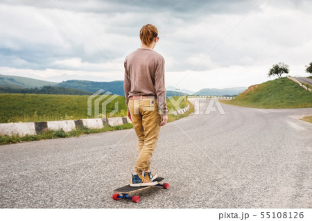 Stylish man rides a longboard on a skateboard along an asphalt country road in the evening against 55108126