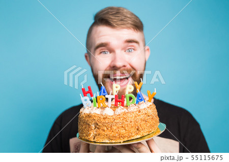Crazy funny positive guy hipster holding a happy birthday cake in his hands standing on a blue Crazy funny positive guy hipster holding a happy birthday cake in his hands standing on a blue 55115675