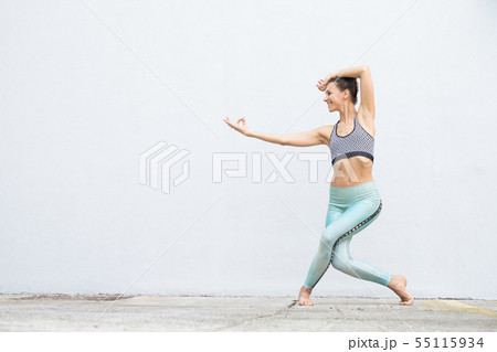 Fit sporty active girl in fashion sportswear doing yoga fitness exercise in front of gray wall 55115934