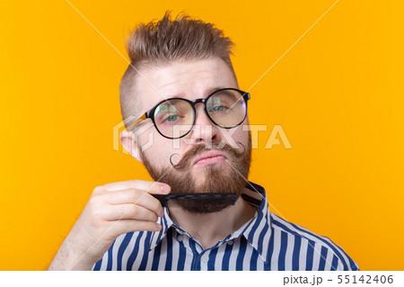 Portrait of a funny handsome young male hipster with a mustache and a beard combing his mustache on 55142406