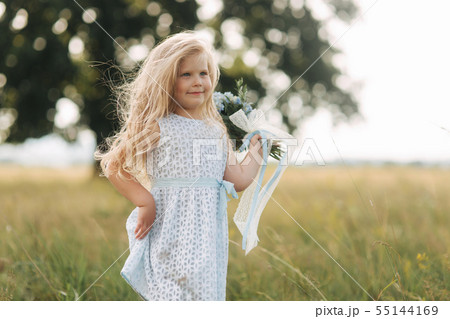 Little girl in sky blue dress stand in field in front of big tree 55144169