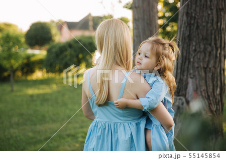 Young beautiful woman with her little cute daughter. Young daughter hugs mother in summer park Young beautiful woman with her little cute daughter. Young daughter hugs mother in summer park 55145854