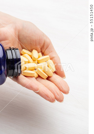 Female hand holds yellow pills on a white table background next to a jar. Concept of treatment of Female hand holds yellow pills on a white table background next to a jar. Concept of treatment of 55151450