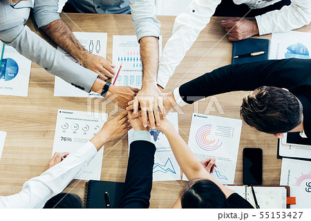 Colleagues stacking hands above table with papers 55153427
