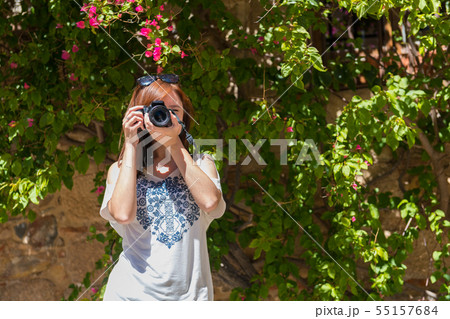 A young woman with reddish hair takes photographs with her camera next to a wall covered with 55157684