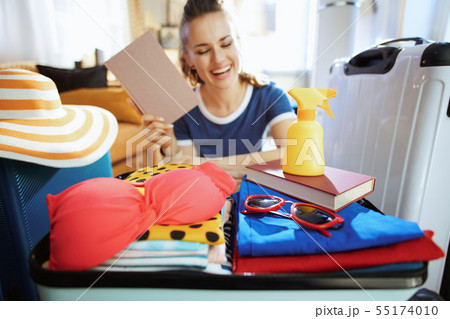 Closeup on open suitcase ready for vacation and woman with book Closeup on open suitcase ready for vacation and woman with book 55174010