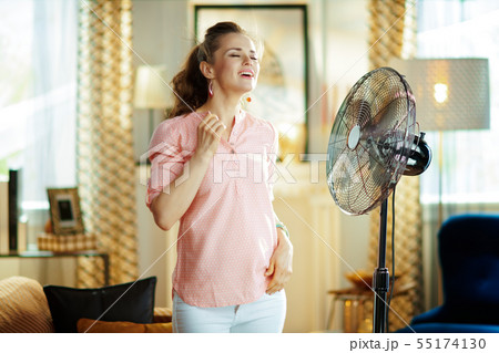 smiling modern woman enjoying freshness in front of fan smiling modern woman enjoying freshness in front of fan 55174130