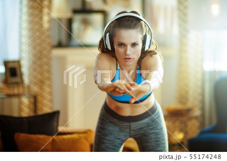 young woman in headphones at modern home stretching 55174248