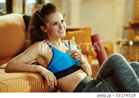 smiling woman with fitness energy bar looking into distance 55174519