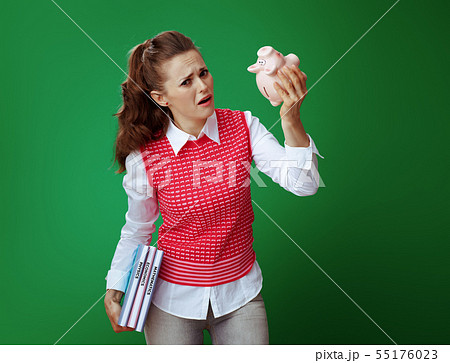 unhappy student woman with textbooks shaking pink piggy bank 55176023