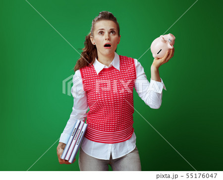learner woman with textbooks shaking pink piggy bank and looking learner woman with textbooks shaking pink piggy bank and looking 55176047