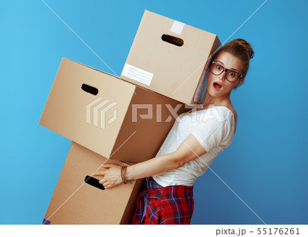 shocked modern woman holding pile of cardboard boxes on blue 55176261