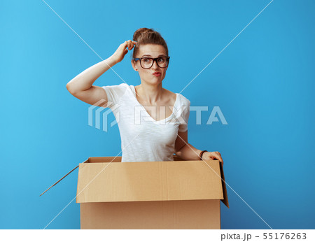 pensive modern woman in white t-shirt in cardboard box on blue pensive modern woman in white t-shirt in cardboard box on blue 55176263