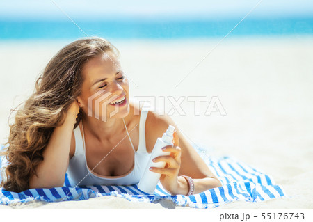 woman with SPF laying on striped towel on ocean shore 55176743