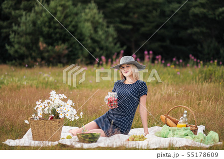 Young attractive woman in a blue dress at an outdoor picnic. A basket with daisies, watermelon 55178609