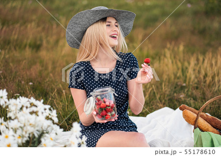 Young attractive woman in a blue dress at an outdoor picnic. A basket with daisies, watermelon Young attractive woman in a blue dress at an outdoor picnic. A basket with daisies, watermelon 55178610