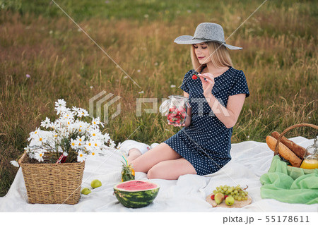 Young attractive woman in a blue dress at an outdoor picnic. A basket with daisies, watermelon 55178611