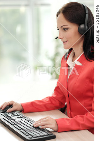 A young attractive woman in a red jacket sitting on a desk at the head of a executive in a red 55183046