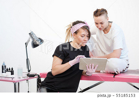 Professional tattoo master woman shows sketches on the tablet to the client girl. Discussion future Professional tattoo master woman shows sketches on the tablet to the client girl. Discussion future 55185153