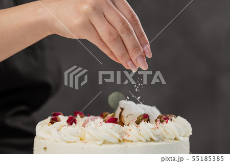 The condater sprinkles the cake with grated almonds and coconut. Close-up of a hand and pouring The condater sprinkles the cake with grated almonds and coconut. Close-up of a hand and pouring 55185385
