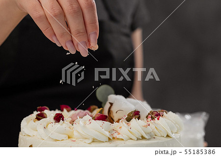 The condater sprinkles the cake with grated almonds and coconut. Close-up of a hand and pouring The condater sprinkles the cake with grated almonds and coconut. Close-up of a hand and pouring 55185386