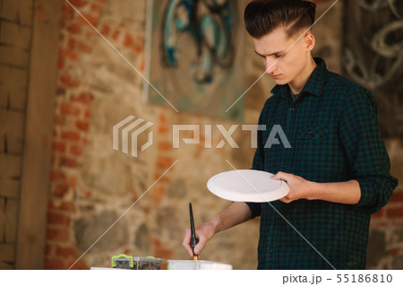 Potter making ornament on ceramic plate. Professional male potter draw a pencil on ceramic product Potter making ornament on ceramic plate. Professional male potter draw a pencil on ceramic product 55186810