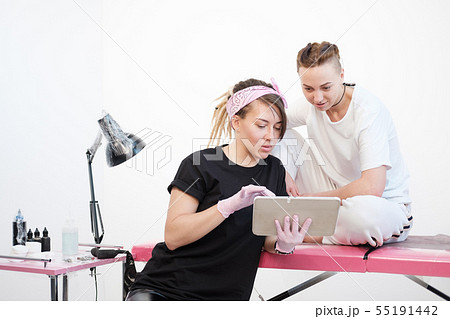 Professional tattoo master woman shows sketches on the tablet to the client girl. Discussion future 55191442