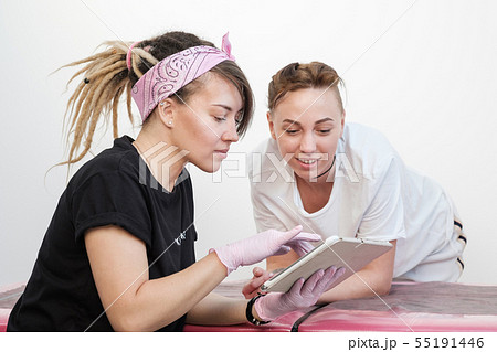 Professional tattoo master woman shows sketches on the tablet to the client girl. Discussion future Professional tattoo master woman shows sketches on the tablet to the client girl. Discussion future 55191446